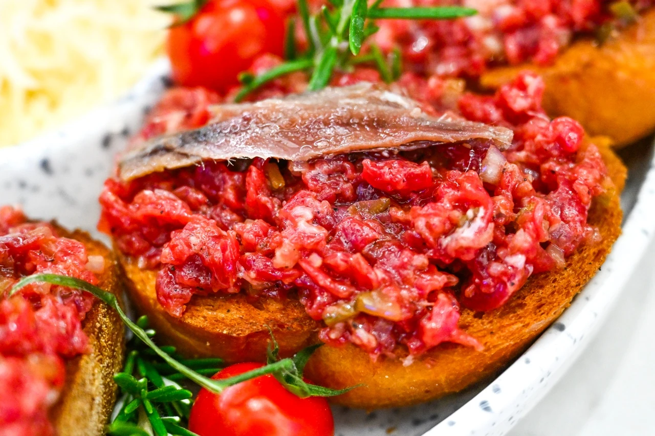 Tatar Jurka Sobieniaka Grzanki z tatarem wołowym, udekorowane filetami z anchois oraz gałązkami świeżego rozmarynu, podane w towarzystwie pomidorków koktajlowych.