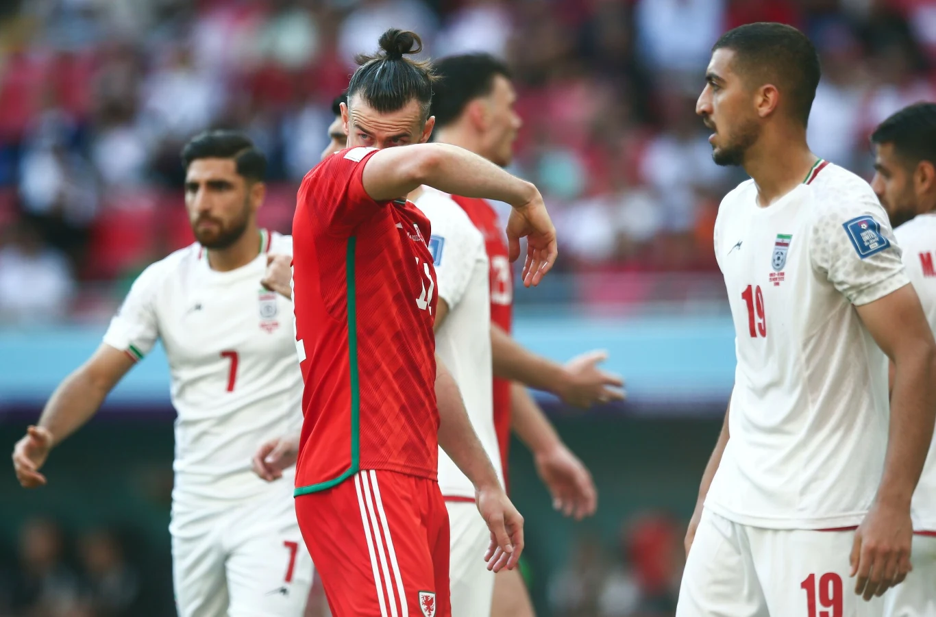 Mecz Walii z Iranem na poprzednim mundialu 2022. Katarskie stadiony były klimatyzowane Piłkarz w czerwonym stroju ocierający twarz przed zawodnikami drużyny w białych strojach podczas meczu piłki nożnej.