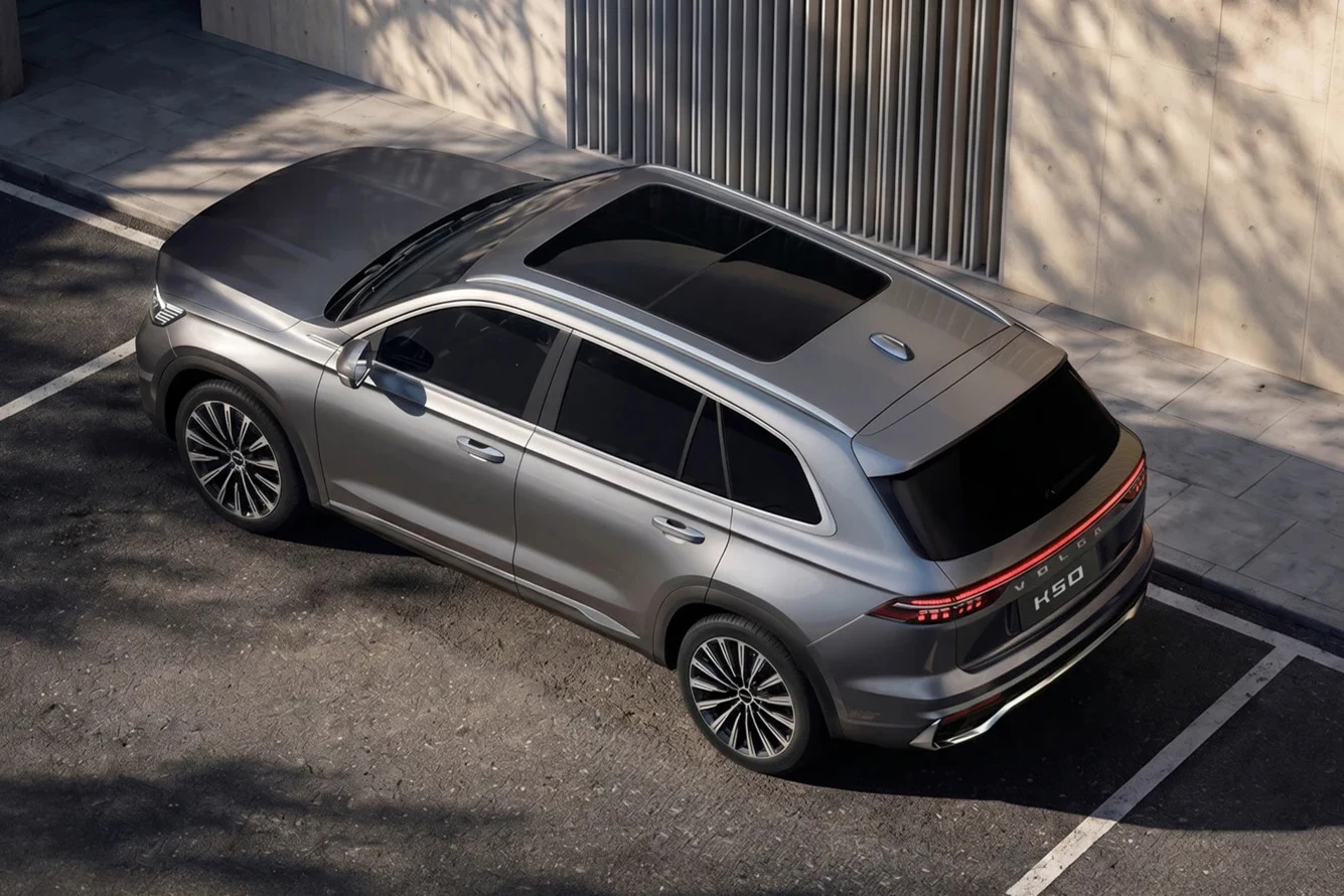 Srebrny SUV z panoramicznym dachem i przyciemnianymi szybami zaparkowany na ulicy obok budynku z pionowymi żaluzjami.