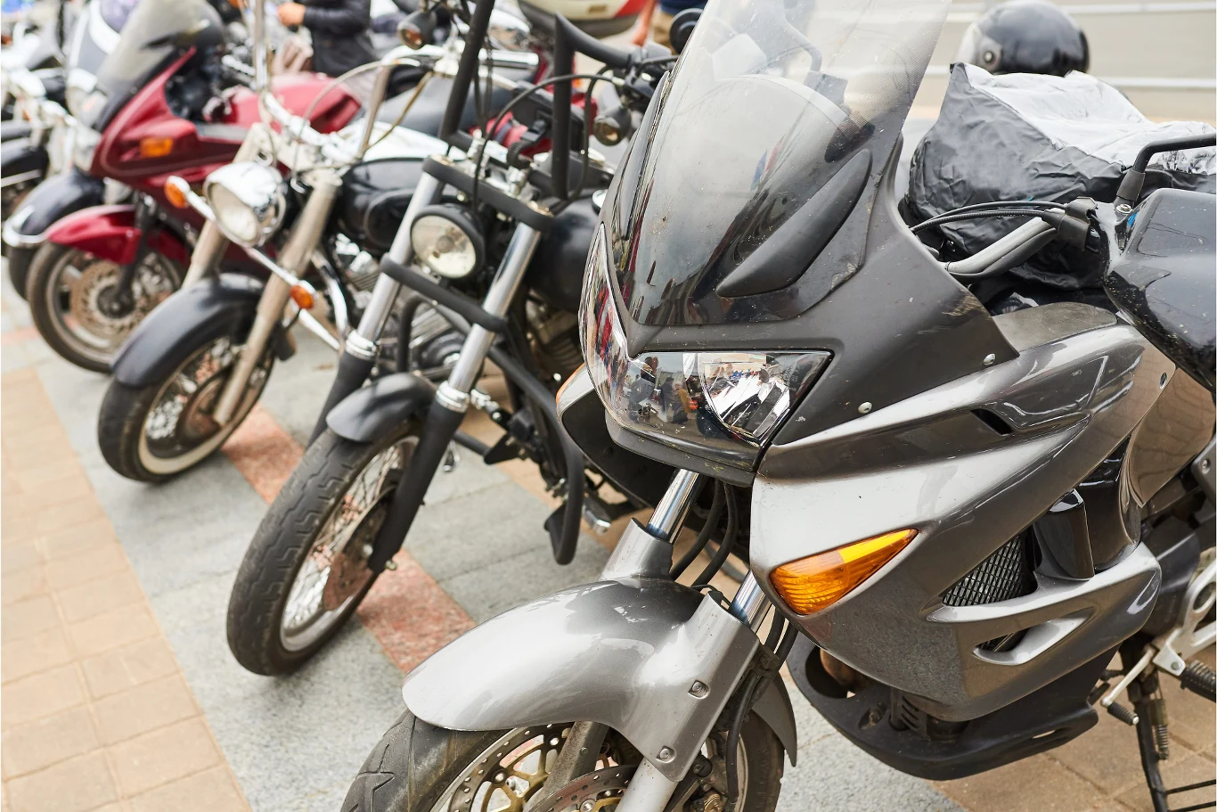 Rząd zaparkowanych motocykli ustawionych blisko siebie na chodniku, z przodu wyróżnia się czarny motocykl typu turystycznego.