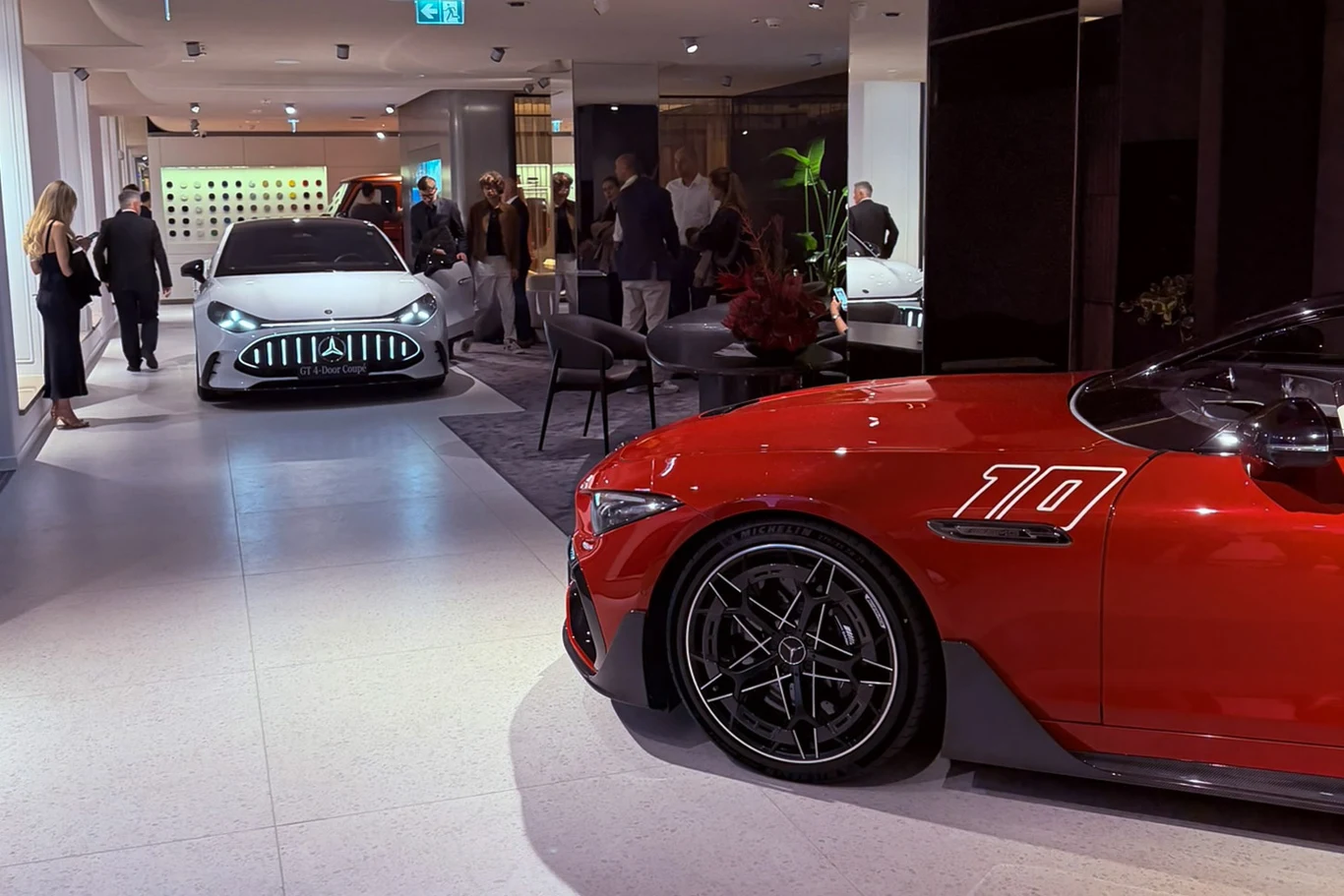 Maybach Atelier w Warszawie Dwa luksusowe samochody sportowe w nowoczesnym, eleganckim salonie wystawowym, w otoczeniu kilku osób dyskutujących i oglądających pojazdy.