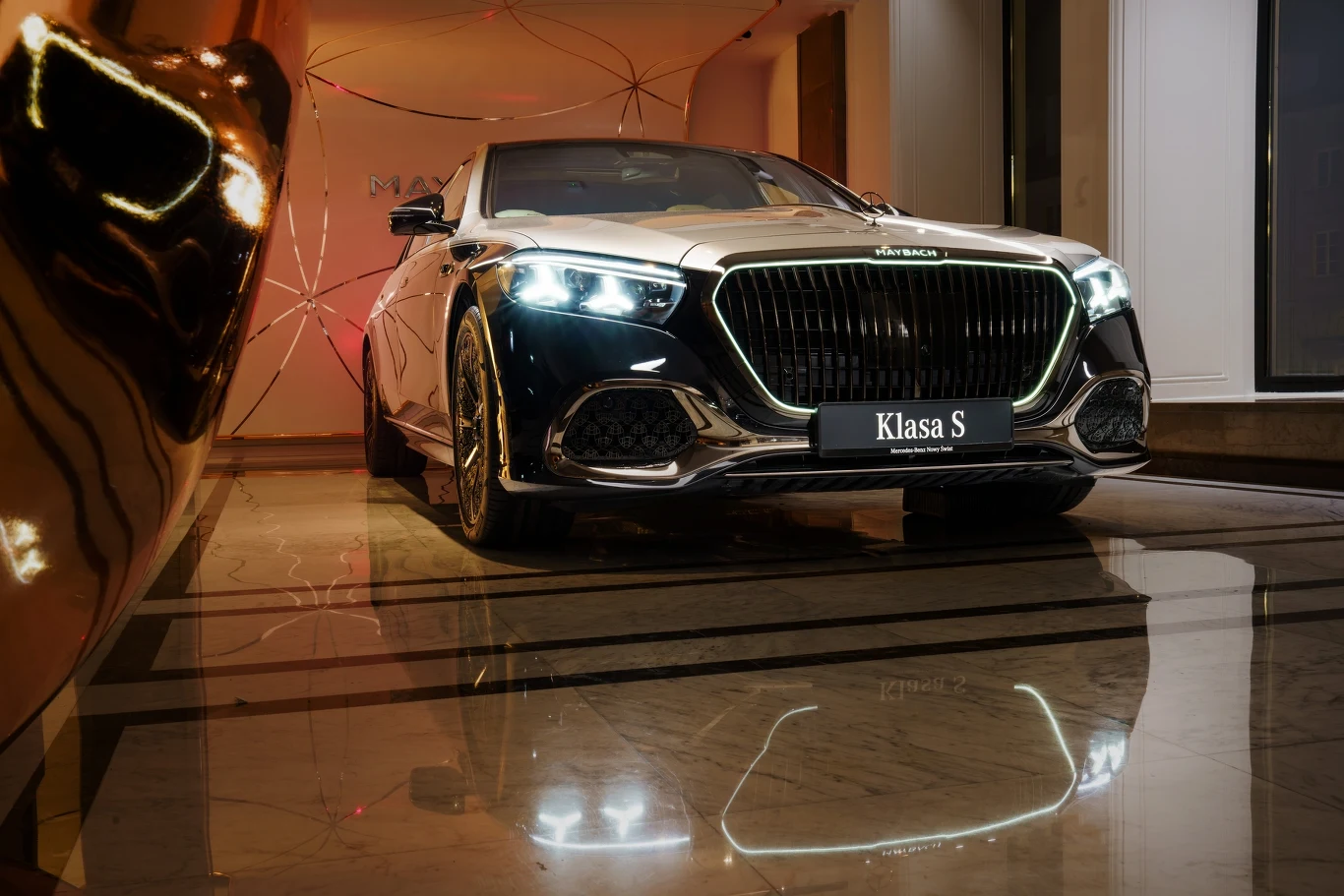 Nowy Mercedes-Maybach Klasy S Luksusowy samochód marki Mercedes-Maybach Klasa S z podświetlonymi reflektorami stoi w eleganckim, nowoczesnym wnętrzu na marmurowej podłodze, odbijając się w jej powierzchni.