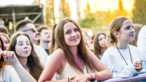 Młode kobiety stojące przy barierce na koncercie, wśród tłumu widoczny uśmiechnięty wyraz twarzy i festiwalowe makijaże.