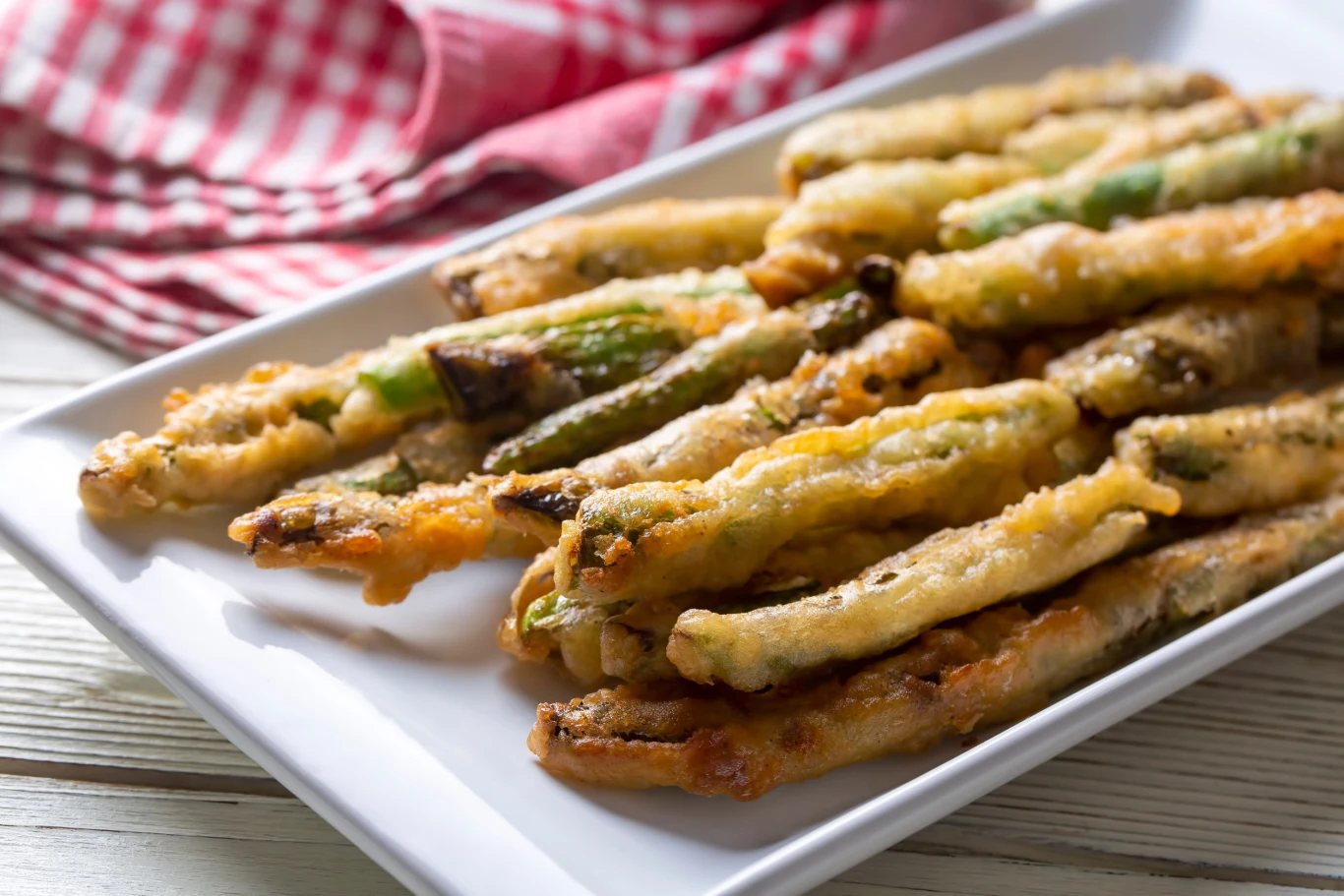 Turkish foods; Crispy baked green beans, fried beans Chrupiące szparagi w złocistej panierce ułożone w rzędach na białym, prostokątnym talerzu.