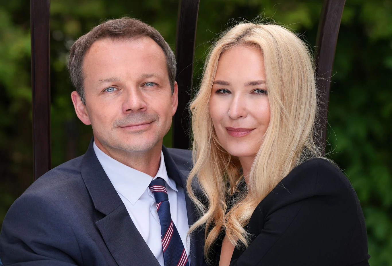 Jak Karolina zareaguje, gdy Bruno zaproponuje jej rozdzielność małżeńską Dwie osoby siedzące blisko siebie, ubrane elegancko; mężczyzna w garniturze i kobieta z długimi blond włosami, oboje patrzą z uśmiechem w stronę aparatu.
