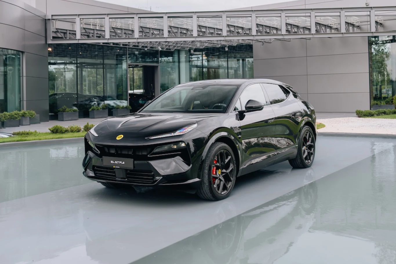 Czarny, sportowy SUV z nowoczesnymi liniami nadwozia i czerwonymi zaciskami hamulców stoi zaparkowany przed przeszklonym budynkiem o futurystycznej architekturze.