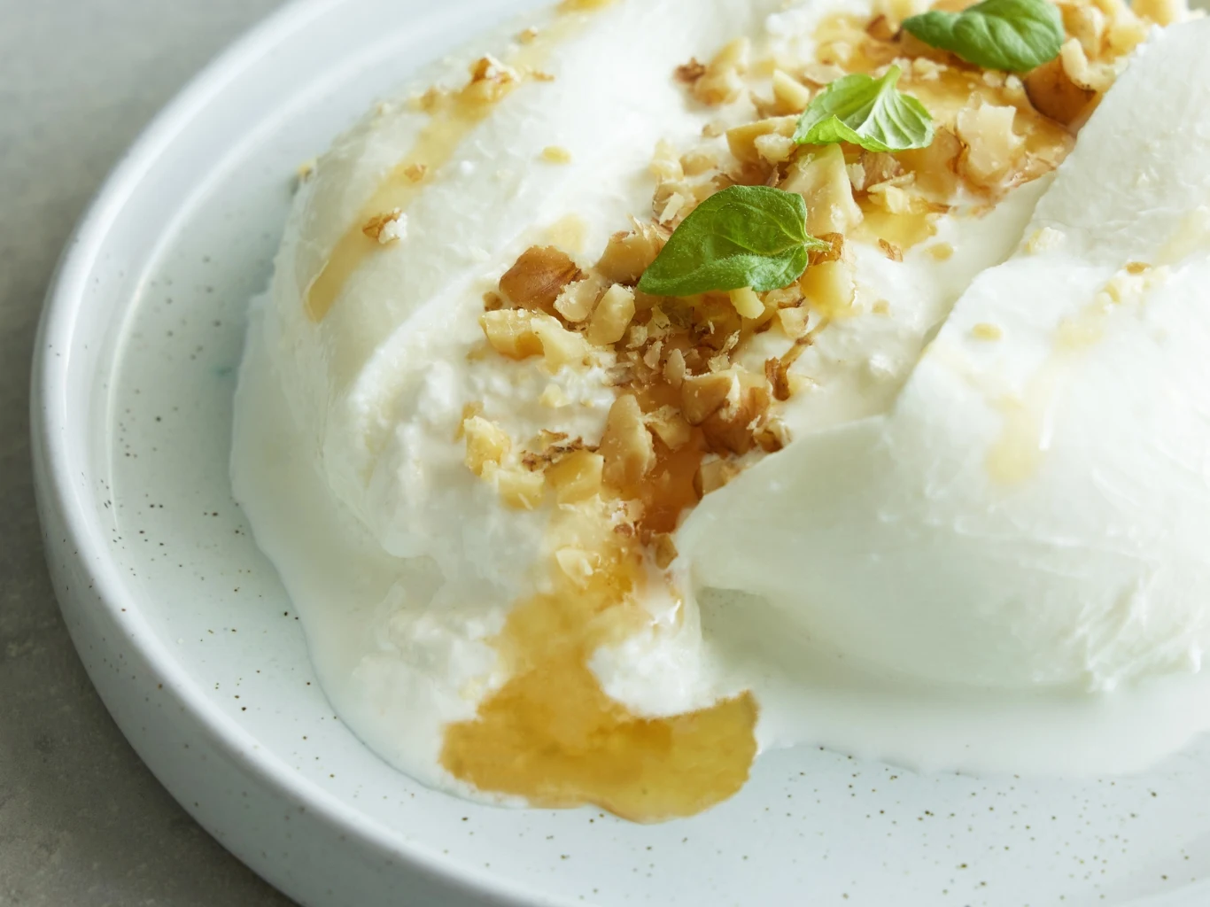 Ten ser jest prawie tak popularny jak mozzarella. Smaczny, zdrowy i można go wykorzystać do wielu dań Porcja burraty z siekanymi orzechami włoskimi, miodem oraz świeżymi listkami bazylii na wierzchu.