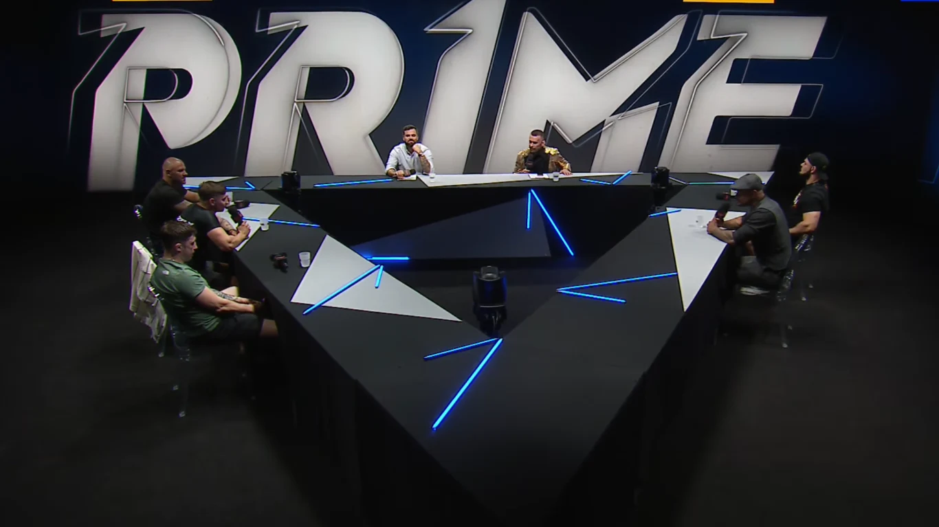 Prime MMA Ośmiu mężczyzn siedzi wokół nowoczesnego, podświetlanego stołu o trójkątnym kształcie, na tle dużego napisu PRIME umieszczonego na ścianie.