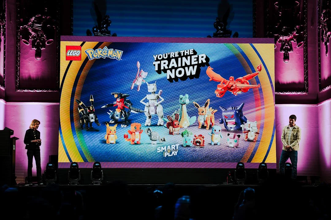 Pokémony „ożyły” dzięki klockom LEGO Ekran z zestawem LEGO Pokémon, logotypami LEGO i Pokémon, hasłem 'You're the trainer now', dwie osoby na scenie