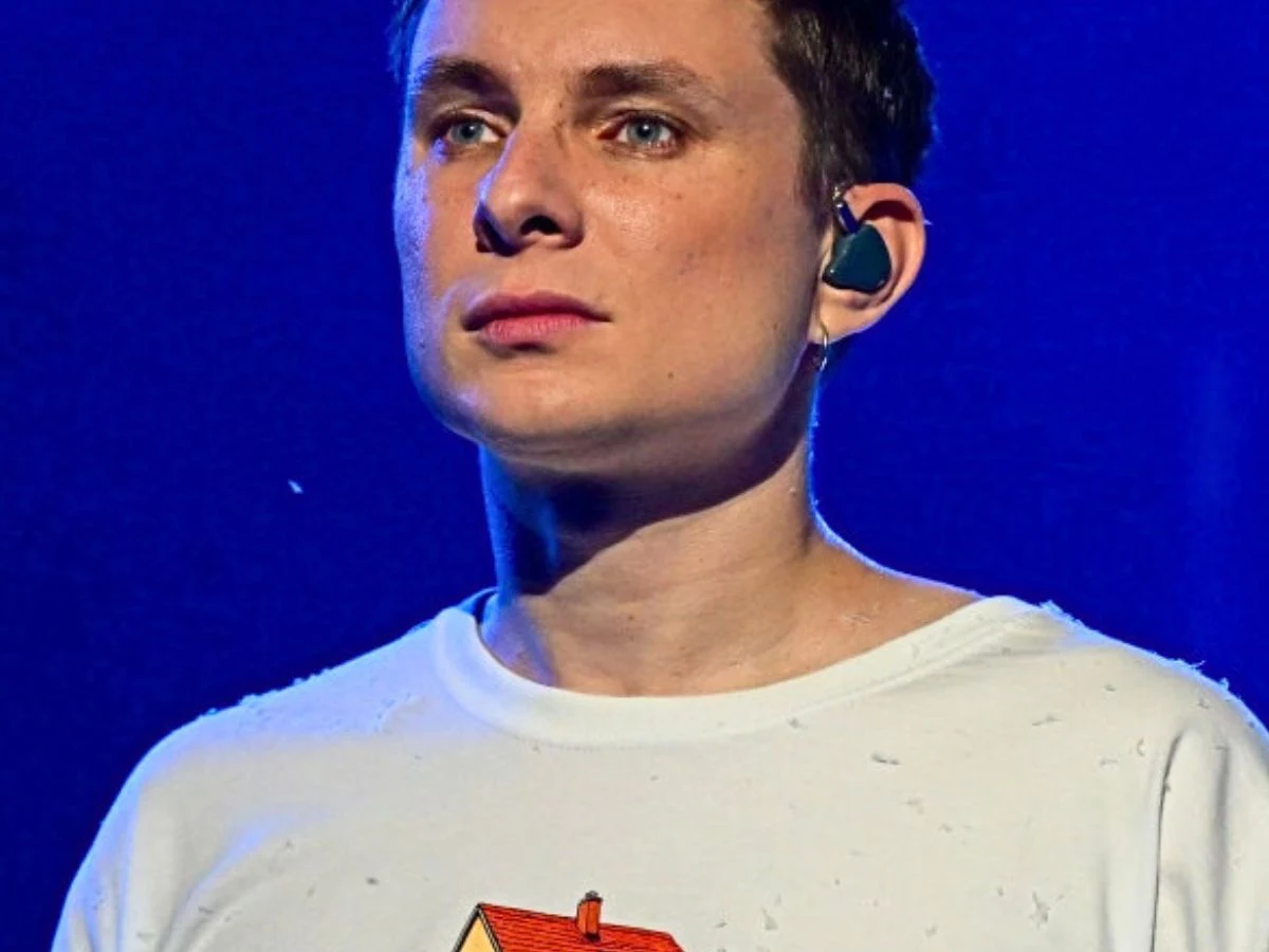 Ralph Kaminski Ralph Kaminski w białym t-shircie, na tle oświetlonym na niebiesko.