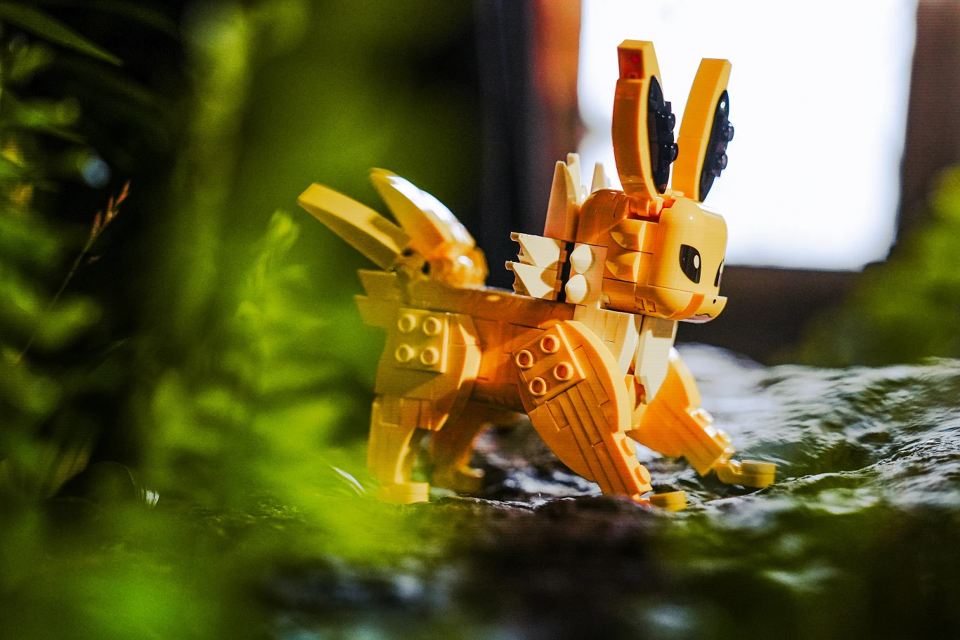 Grupa LEGO i The Pokémon Company od początku zakładały, że nie poprzestaną na kolekcjonerskich figurkach Żółta figurka z klocków przedstawiająca postać o wyrazistych uszach i ogonie, ustawiona na naturalnym podłożu w otoczeniu zieleni.