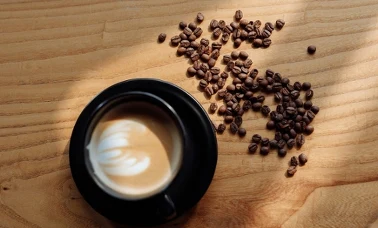 Filiżanka kawy z latte art i rozsypane ziarna kawy na drewnianym blacie