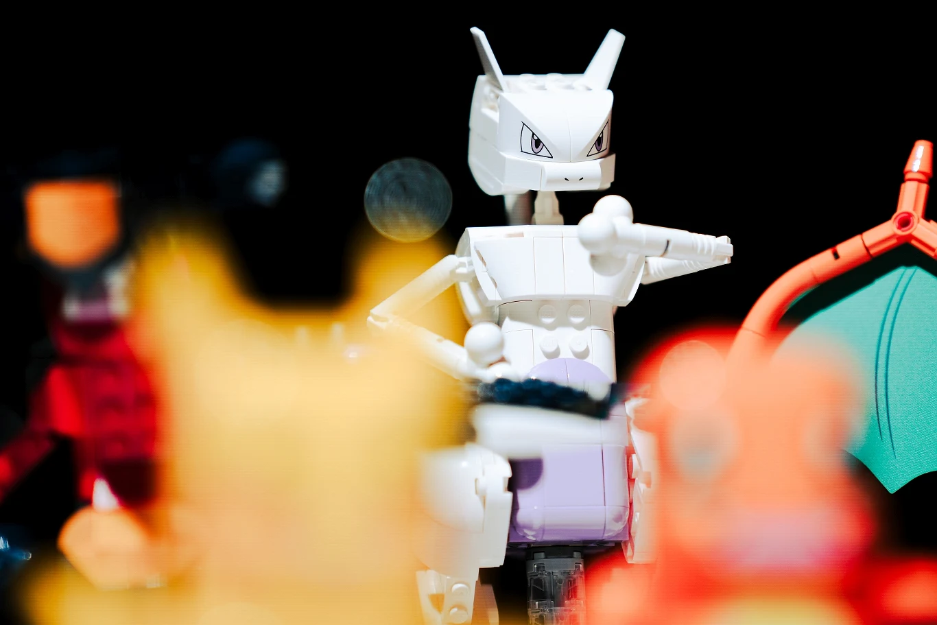 Zestawy klocków LEGO Pokémon SMART Play trafią do sprzedaży 1 sierpnia 2026 roku Biała figurka Mewtwo z klocków, otoczona rozmazanymi postaciami innych Pokémonów, w tym widoczne skrzydło Charizarda po prawej stronie.