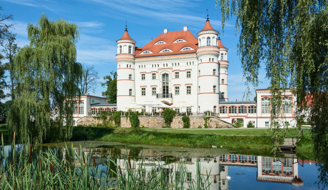 Pałac w Wojanowie na Dolnym Śląsku Pałac w Wojanowie na Dolnym Śląsku, biały budynek z czerwonym dachem i czterema wieżami, odbicie w stawie.