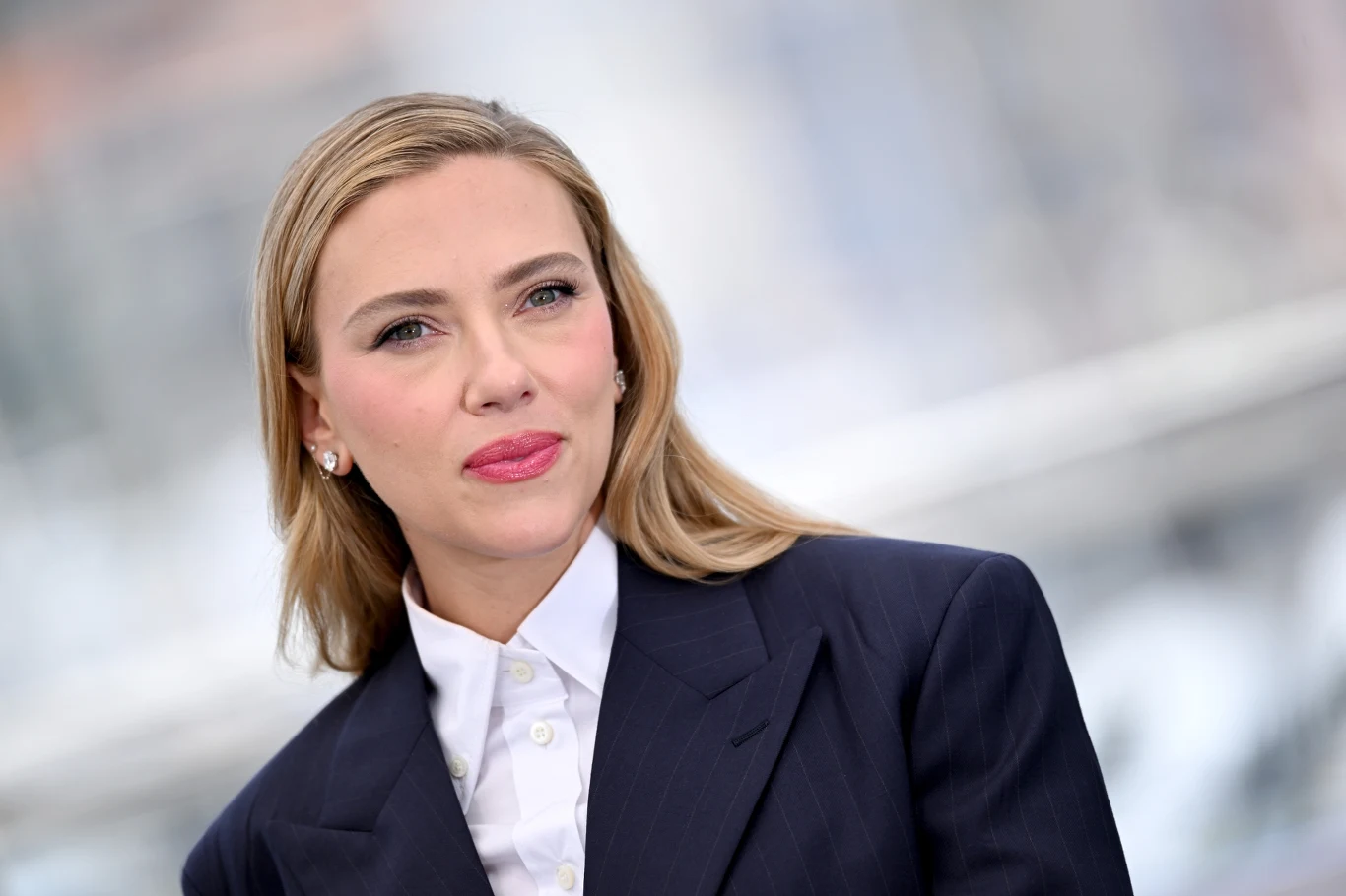 Scarlett Johansson Scarlett Johansson w ciemnym garniturze i białej koszuli, patrzy w obiektyw z delikatnym uśmiechem.