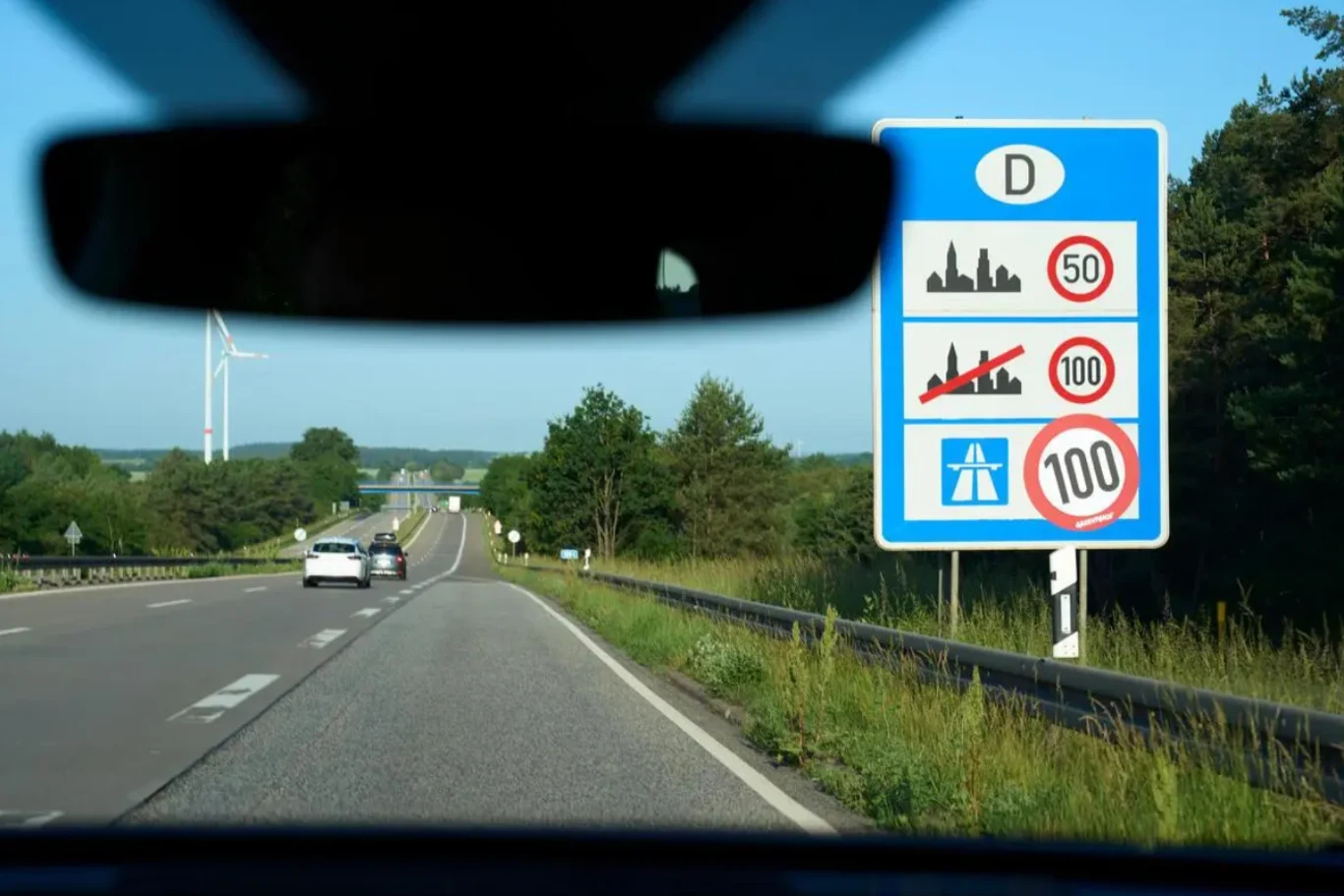 Na 26 odcinkach niemieckich autostrad pojawiło się ograniczenie prędkości do 100 km/h. Samochody na niemieckiej autostradzie z ograniczeniem prędkości do 100 km/h, znak drogowy, zalesiony teren.