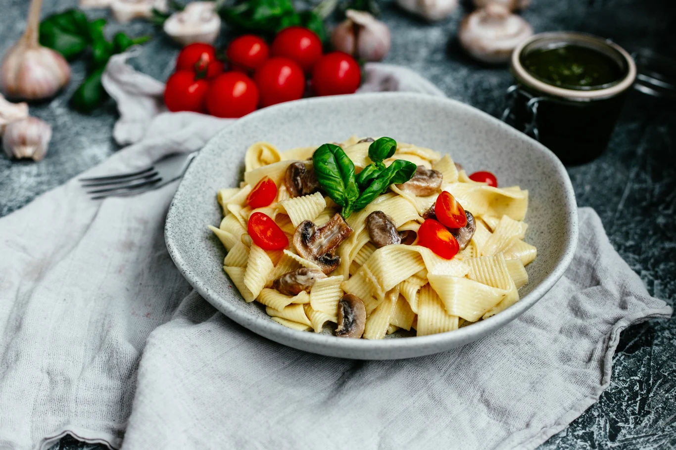 Makaron tagliatelle z pieczarkami oraz kawałkami pomidorów koktajlowych, udekorowany świeżą bazylią.