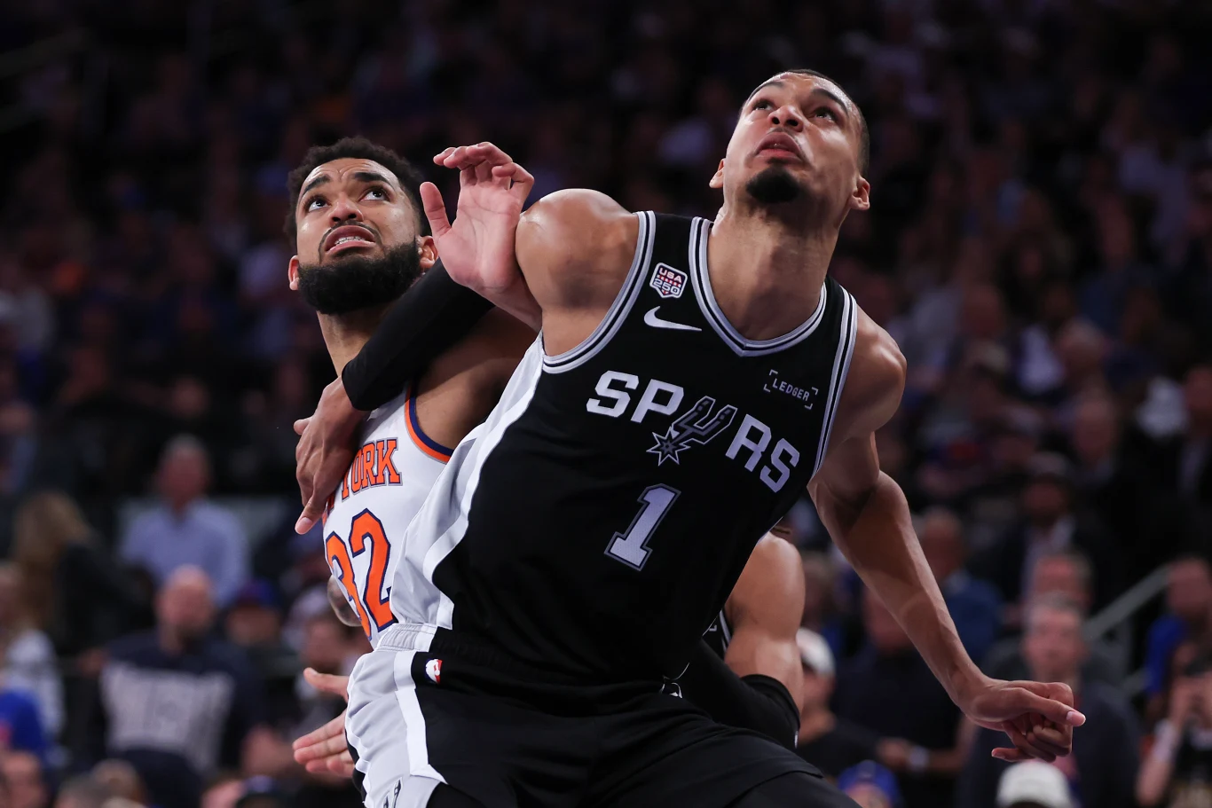 Karl-Anthony Towns i Victor Wembanyama Dwóch koszykarzy walczy o pozycję pod koszem podczas meczu NBA, jeden w czarnym stroju San Antonio Spurs, drugi w białym stroju New York Knicks, skoncentrowani na grze i rywalizacji o piłkę.