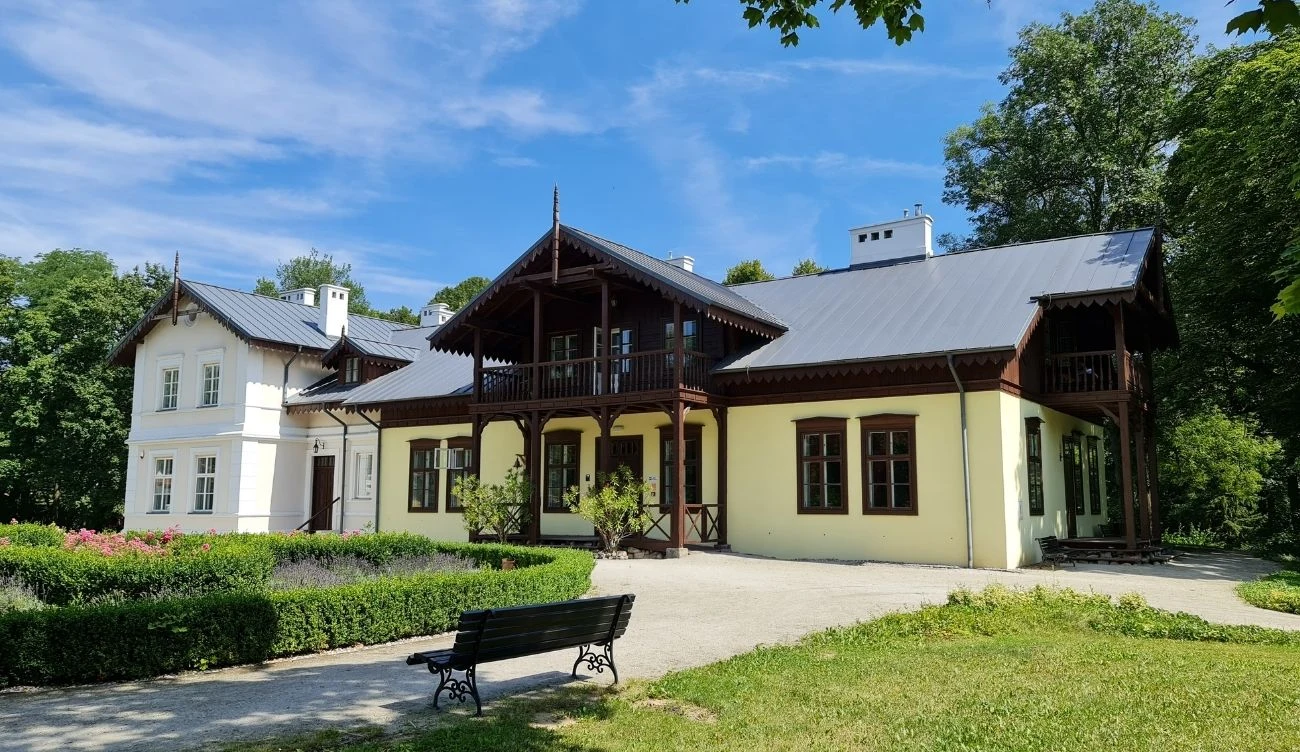 Dwór Orpiszewskich w Kłóbce przyciąga turystów historią i XIX-wiecznym klimatem Dwór Orpiszewskich w Kłóbce z jasną elewacją, drewnianymi detalami, otoczony zielenią, ławka przy alejce.