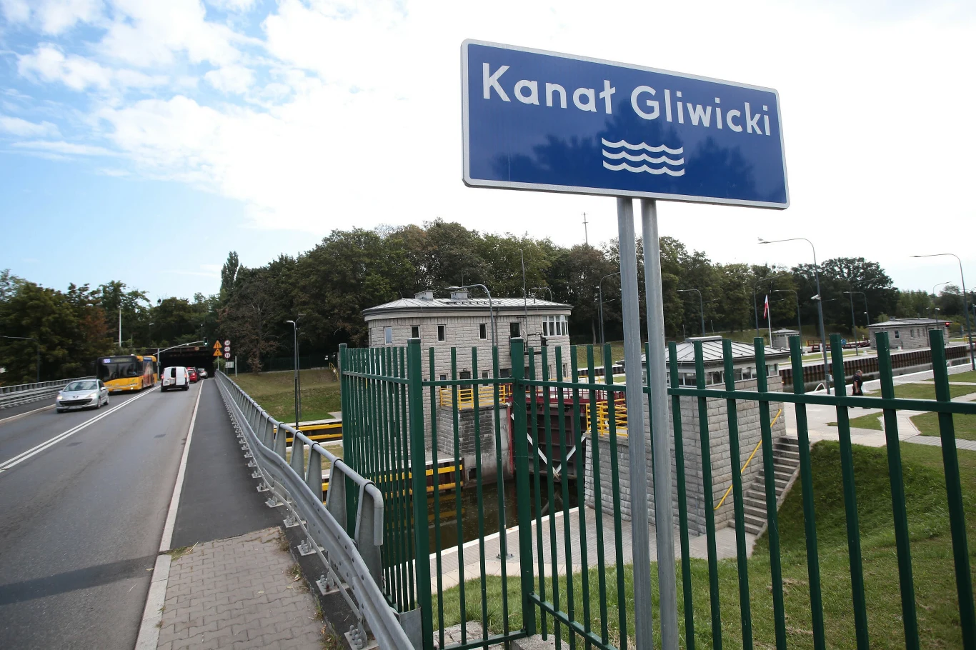 Niegdyś za Kanałem Gliwickim znajdował się zameczek rodu Welczek Niebieska tablica z napisem „Kanał Gliwicki” stoi przy ogrodzeniu kanału wodnego, po lewej stronie biegnie asfaltowa jezdnia z samochodami i autobusem, w tle widoczny budynek sterowni otoczony zielenią.