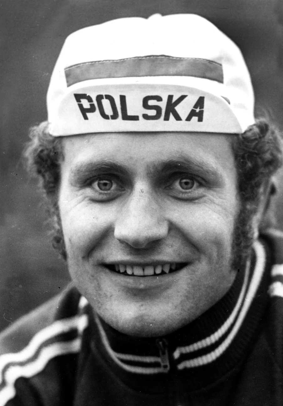 Uśmiechnięty mężczyzna w sportowej bluzie i czapeczce z napisem POLSKA oraz wizerunkiem flagi Polski.