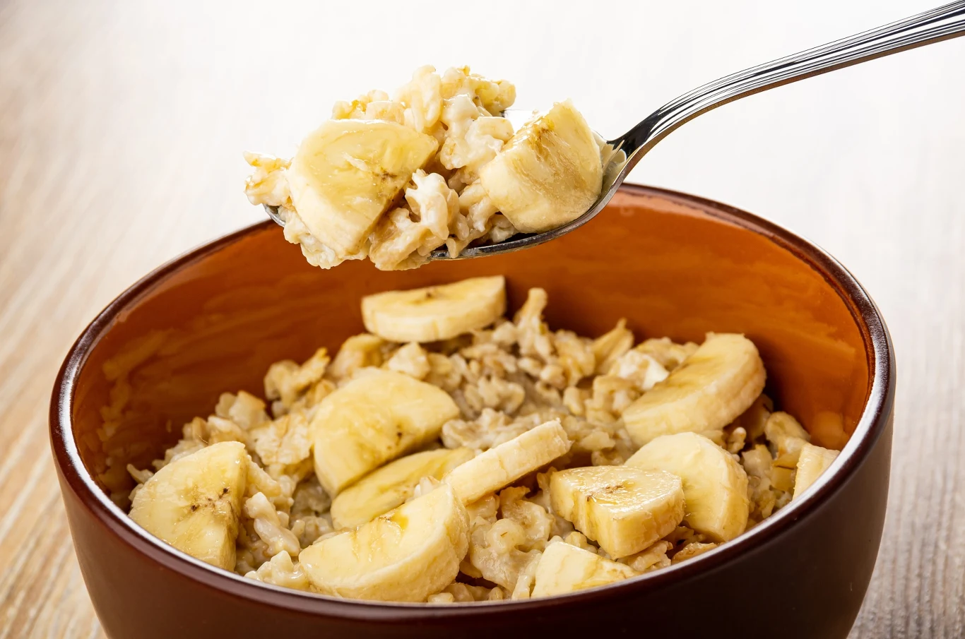 Niektóre produkty mogą sprawić, że owsianka nie będzie już tak zdrowym posiłkiem Owsianka z kawałkami banana w brązowej misce, na łyżce owsianka uniesiona nad miską.