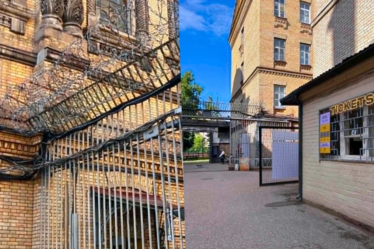 Budynek z żółtej cegły otoczony wysokimi metalowymi ogrodzeniami zwieńczonymi drutem kolczastym, po prawej stronie widoczna kasa biletowa z szyldem TICKETS, a w tle fragment bramy wejściowej oraz fragment dziedzińca.