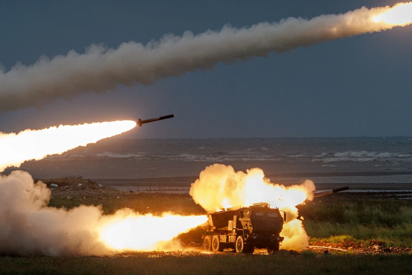 Wyrzutnia HIMARS na Tajwanie wystrzeliwuje rakiety nad Cieśniną Tajwańską, w tle morze i smugi dymu.