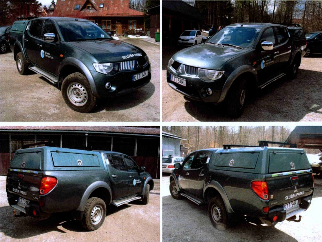 Ciemnozielony pickup Mitsubishi L200 z oznaczeniami Służby Parku, wyposażony w zamykaną zabudowę przestrzeni bagażowej oraz terenowe opony, zaparkowany na utwardzonym placu w otoczeniu budynków i drzew.