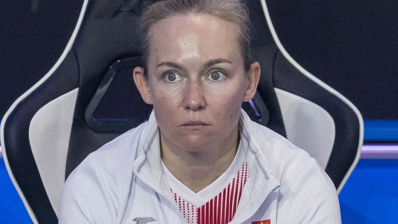 Kobieta w białej sportowej kurtce siedzi na czarnym fotelu gamingowym, skupiona i poważna wyraz twarzy.