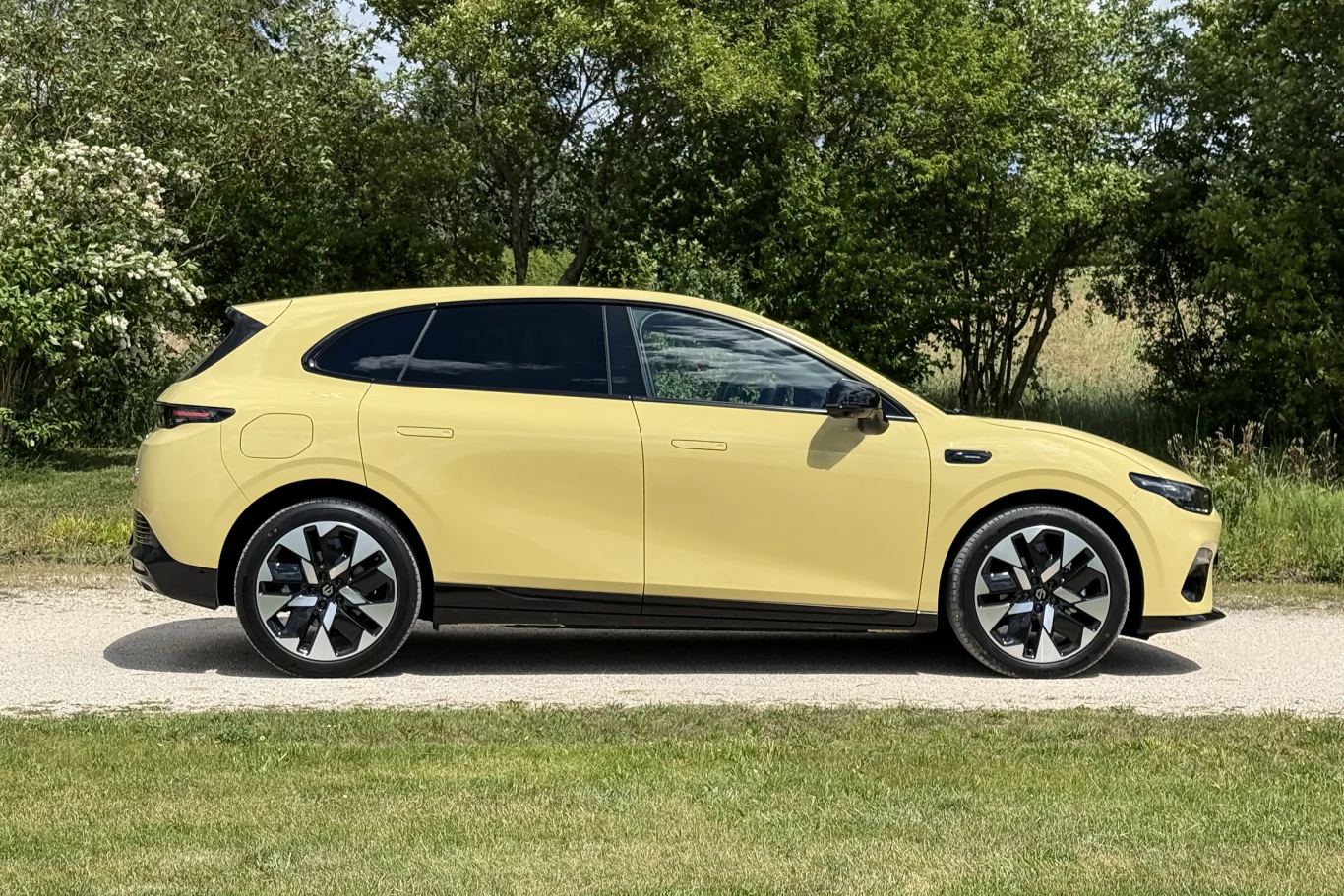 Żółty nowoczesny SUV o dynamicznym wyglądzie nadwozia, duże felgi aluminiowe i przyciemniane szyby, zaparkowany na drodze przy zieleni.