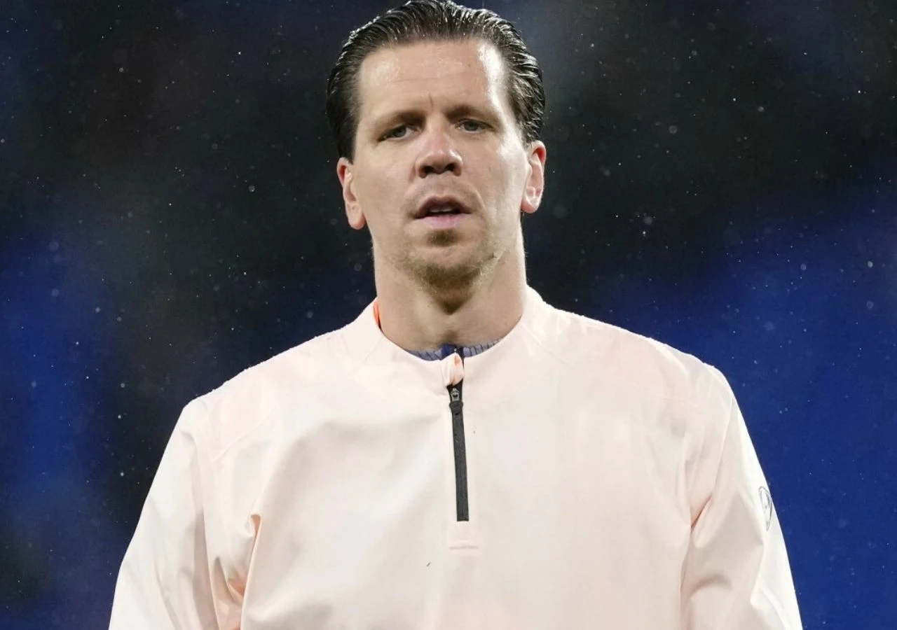 Wojciech Szczęsny Bramkarz Wojciech Szczęsny w jasnej sportowej bluzie, tło niebieskie, rozmyte. Ma smutny wyraz twarzy