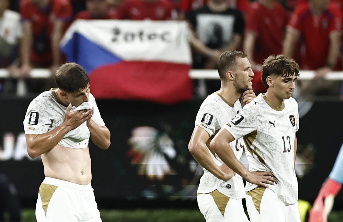 Reprezentacja Czech Trzech rozczarowanych piłkarzy w białych strojach na tle czeskiej flagi oraz kibiców ubranych na czerwono.