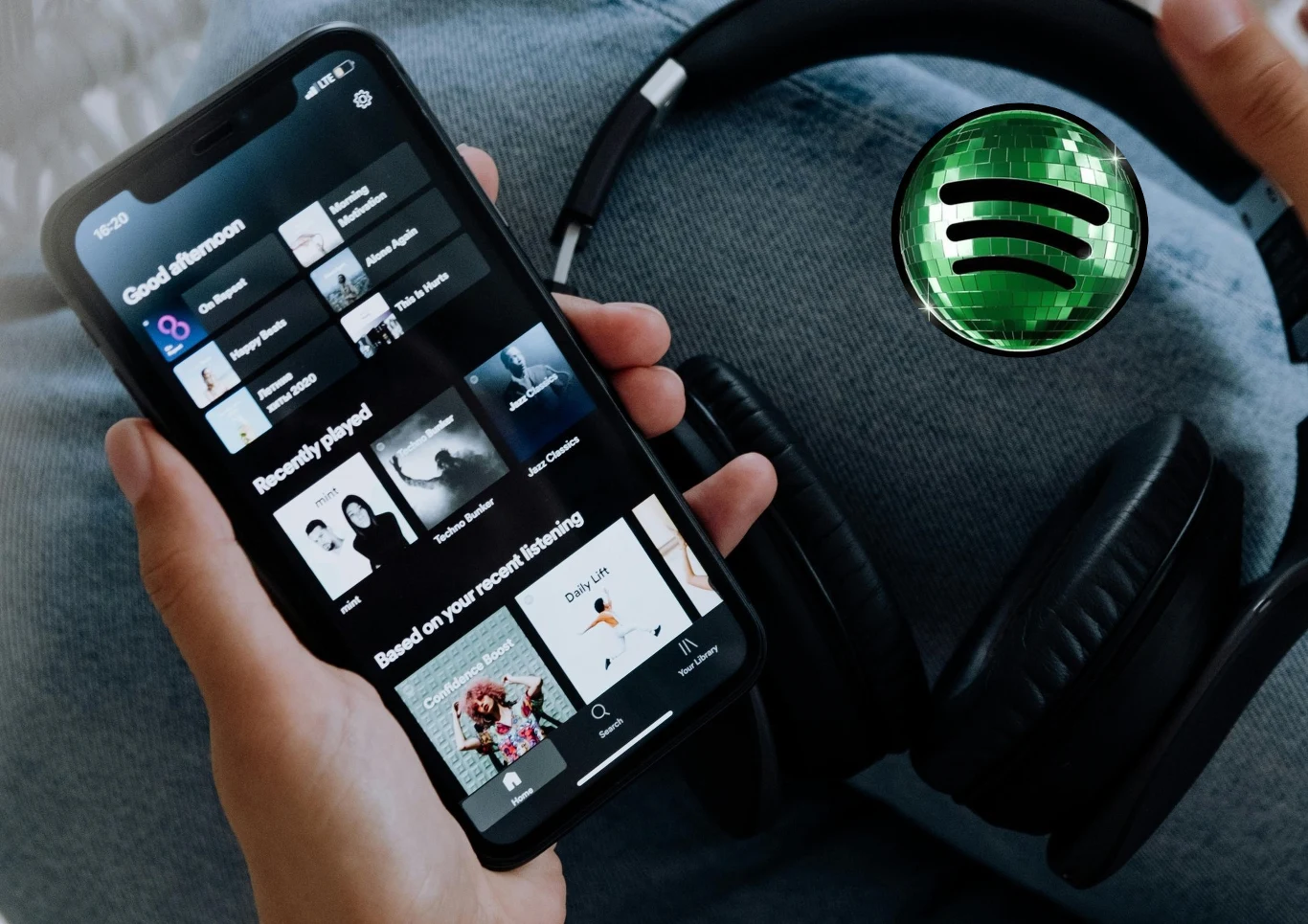 Smartfon z otwartą aplikacją Spotify, czarne słuchawki na nogach, obok widoczne logo Spotify.