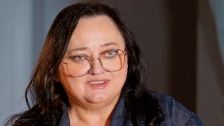 Kobieta o ciemnych włosach i okrągłych okularach, uśmiechnięta, ubrana w granatową marynarkę, spogląda w kierunku kamery.