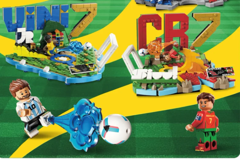 Dwie figurki z klocków LEGO w strojach piłkarskich, jedna kopiąca piłkę, otoczone stadionami z elementami tematycznymi nawiązującymi do znanych zawodników, z dużymi literami VINIJR i CR7 w tle.