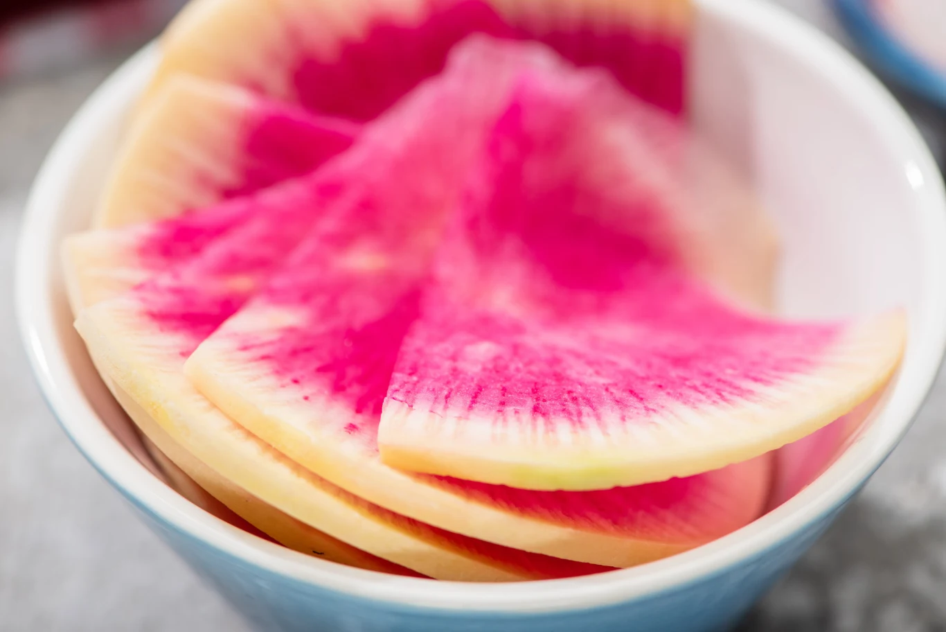 close up view of fresh watermelon radish slices in bowl Plasterki rzodkiewki arbuzowej w białej miseczce, widoczne różowe wnętrze i jasna skórka.