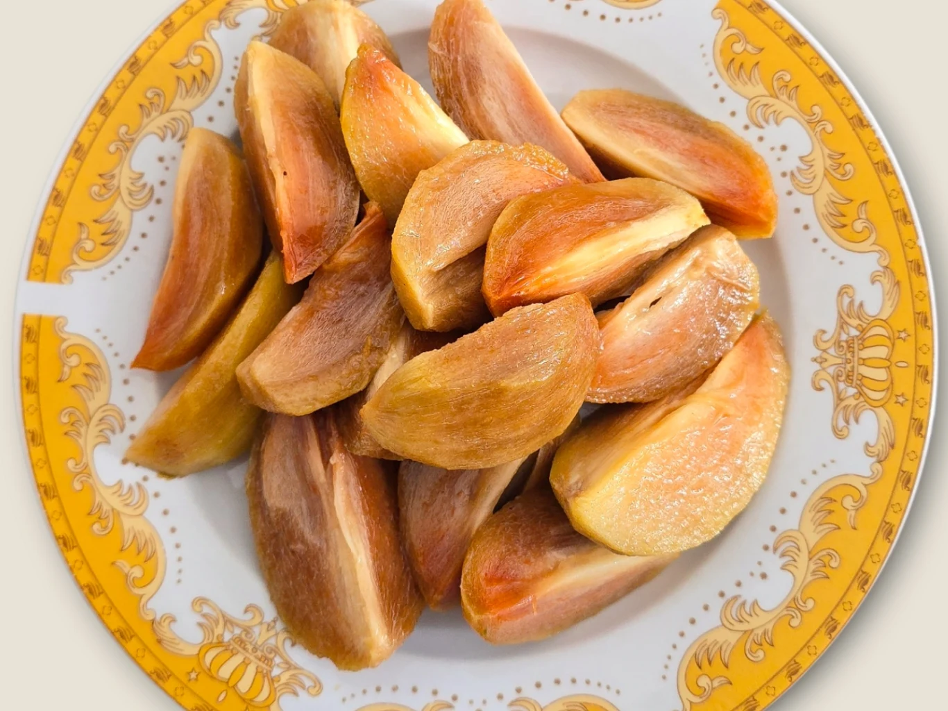 Miąższ tego egzotycznego owocu w smaku przypomina toffi. Przyspiesza metabolizm. Pokrojone kawałki sapodilli o brązowo-pomarańczowej skórce i jasnym miąższu na talerzu z żółtym wzorem.