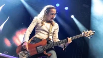 Kobieta grająca na gitarze basowej podczas dynamicznego występu na scenie, oświetlonej kolorowymi reflektorami.