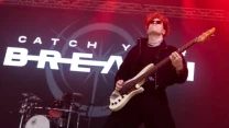 Gitarzysta grający na scenie podczas koncertu zespołu Catch Your Breath, w tle widoczny perkusista oraz duży napis z nazwą zespołu na telebimie.