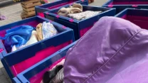 Plastikowe pojemniki wypełnione różnokolorowymi ubraniami ustawione na zewnątrz na chodniku.