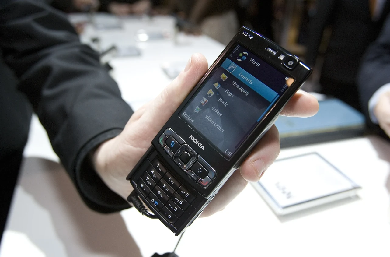 Nokia N95 Czarna Nokia N95 z menu na wyświetlaczu, trzymana w dłoni mężczyzny w ciemnym rękawie.