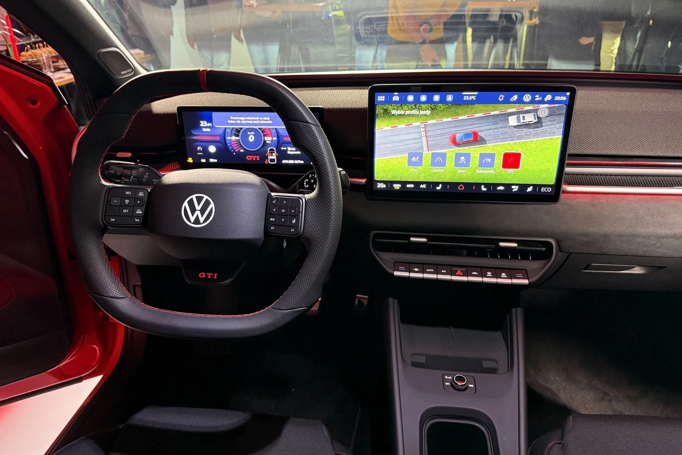 Z wnętrzem utrzymanym w czarnym kolorze kontrastują czerwone detale i przeszycia. Wnętrze nowoczesnego samochodu marki Volkswagen z wielofunkcyjną kierownicą, cyfrowym zestawem wskaźników oraz dużym, dotykowym ekranem systemu multimedialnego na centralnej konsoli.