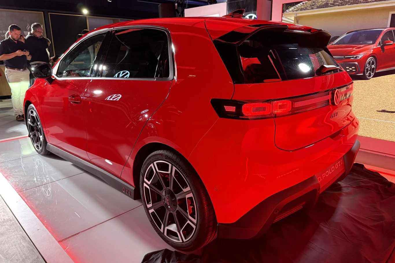Volkswagen ID.Polo GTI generuje 226 KM i 290 Nm. Napęd trafia na przednie koła. Czerwony hatchback o sportowym wyglądzie, z przyciemnionymi szybami, charakterystycznymi felgami oraz tylnym spojlerem, prezentowany w jasnym oświetleniu wystawowym.