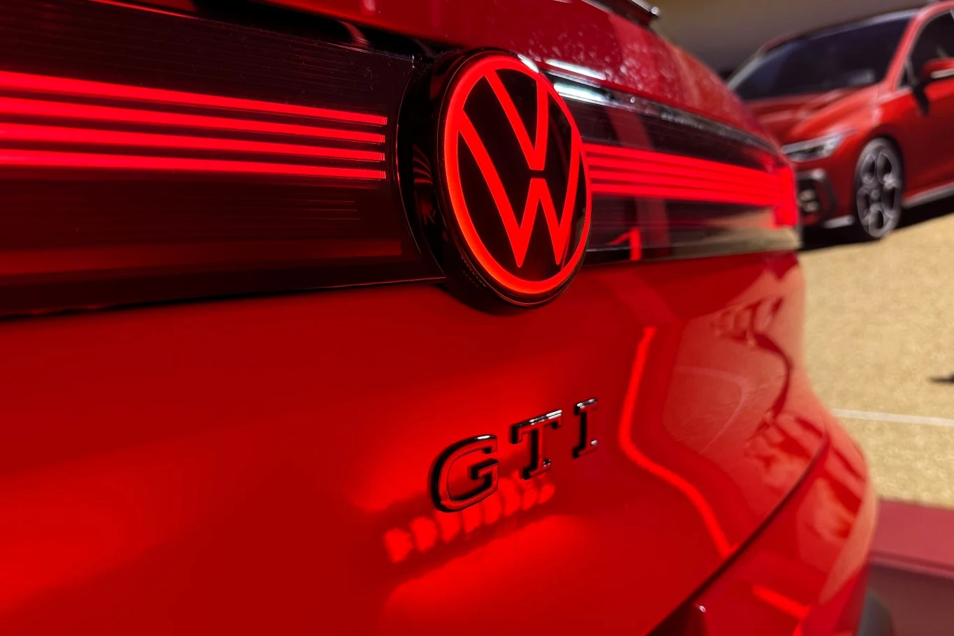 W standardzie Volkswagen ID.Polo GTI wyposażony jest w adaptacyjne zawieszenie DCC. Czerwony Volkswagen GTI z wyraźnie widocznym emblematem GTI i charakterystycznym logotypem marki, a w tle drugi samochód tej samej marki.