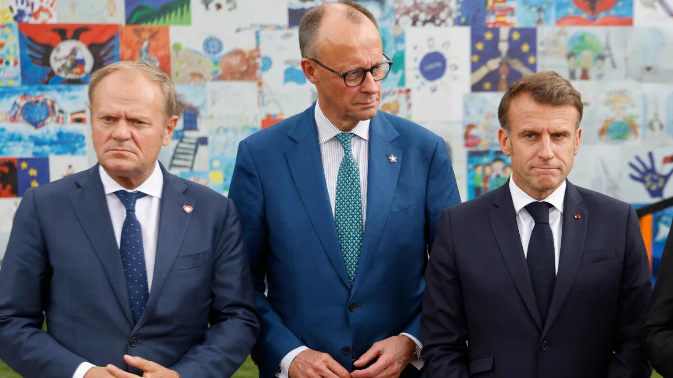 Donald Tusk, Friedrich Merz i Emmanuel Macron w garniturach stoją obok siebie na tle ściany z rysunkami, zdjęcie ilustracyjne.