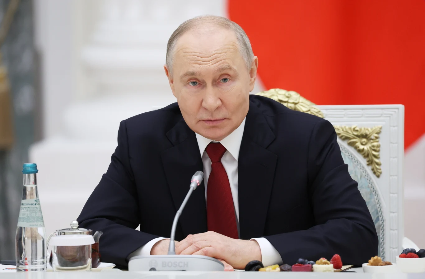 Władimir Putin w garniturze i bordowym krawacie siedzi przy stole podczas spotkania z żołnierzami.