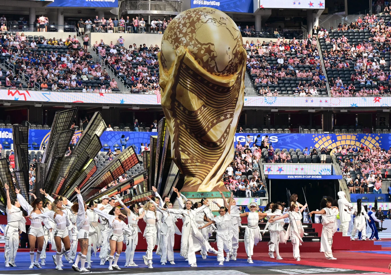 Ceremonia otwarcia mundialu 2026 w Los Angeles Grupa tancerzy w białych strojach wykonuje choreografię przed ogromną repliką Pucharu Świata FIFA na stadionie wypełnionym kibicami.