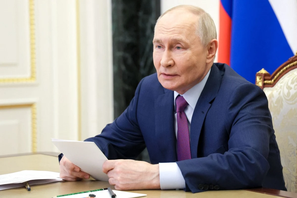 Władimir Putin w garniturze przy stole, trzyma w rękach plik kartek, patrząc przed siebie