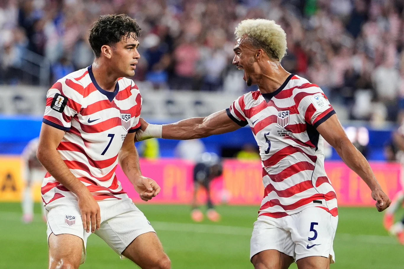 Giovanni Reyna i Antonee Robinson Dwóch piłkarzy w biało-czerwonych koszulkach drużyny USA świętuje zdobycie bramki na boisku podczas meczu, jeden z nich wyraża radość, energicznie gestykulując w kierunku drugiego.